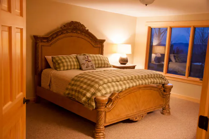 A bedroom with a wooden bed, checkered blanket, and a large window.