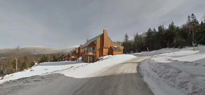 A snow-covered road leads to a lodge with a chimney.